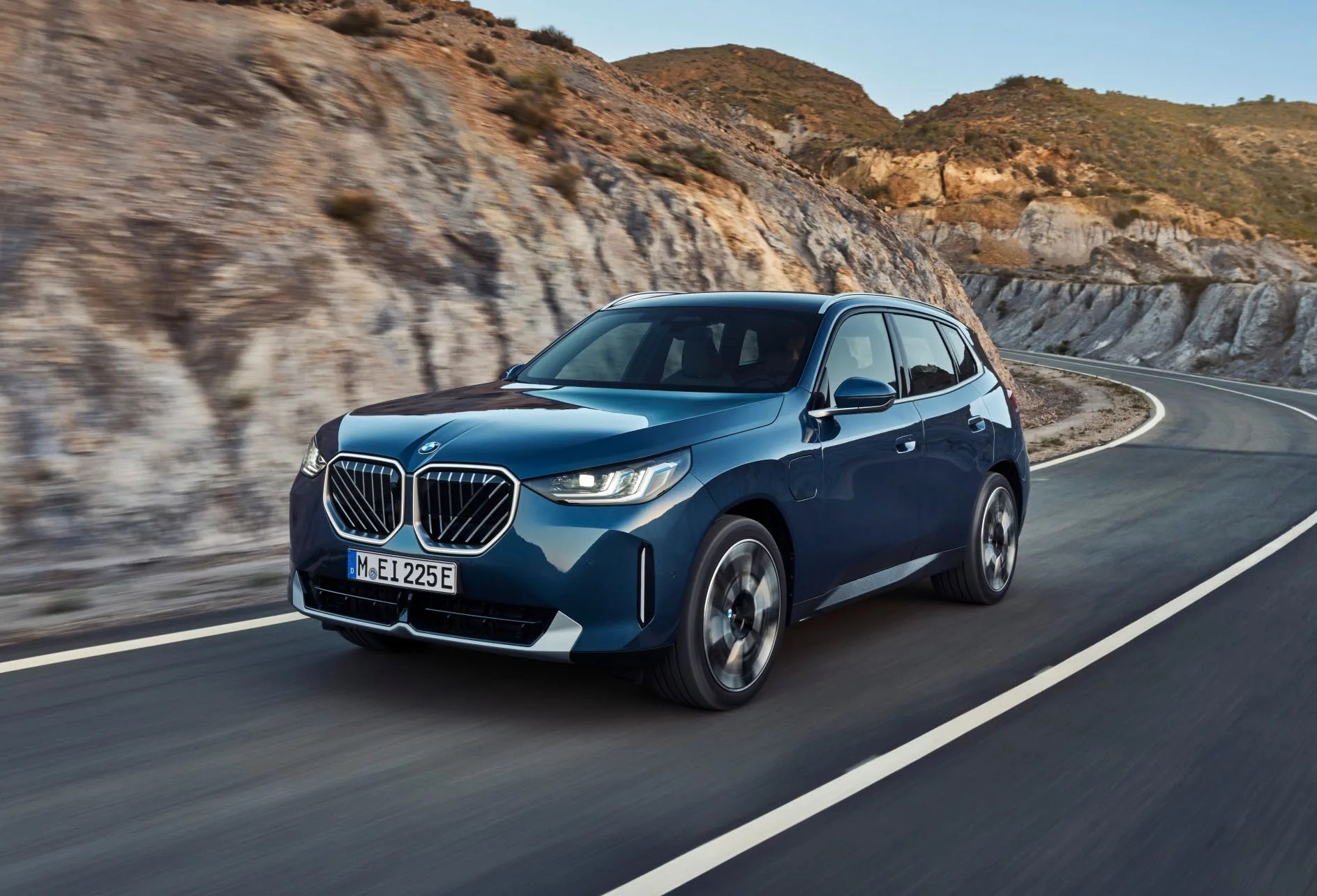 2025 BMW X3 in blue driving on road in front of rock canyon walls