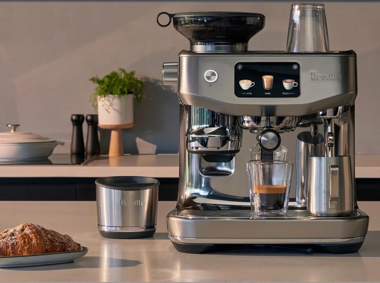 Breville Oracle Jet espresso machine sitting on kitchen countertop next to tap box and a croissant