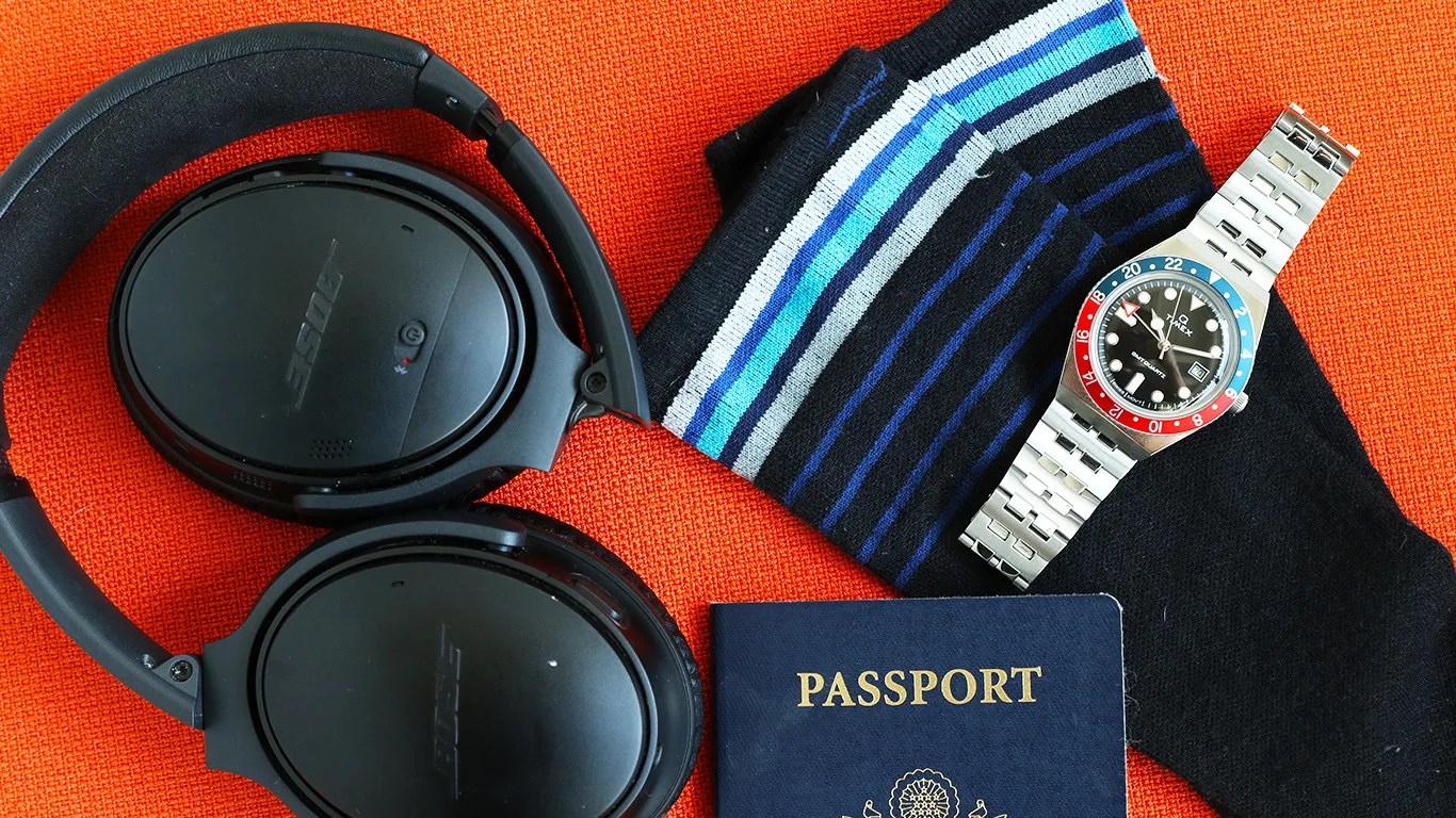 headphones a watch a passport and compression stockings against an orange background