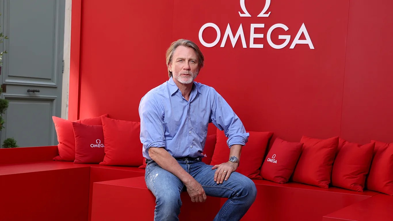 daniel craig sits in a red omega branded room