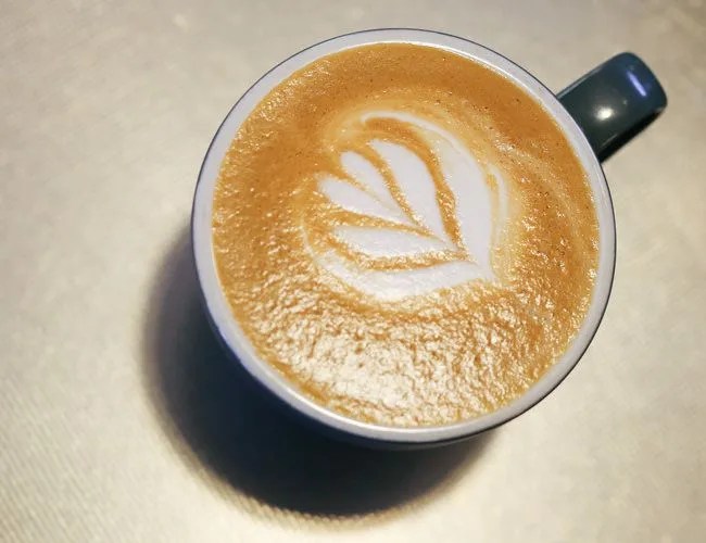 Flat white coffee drink in mug on table with rose pattern