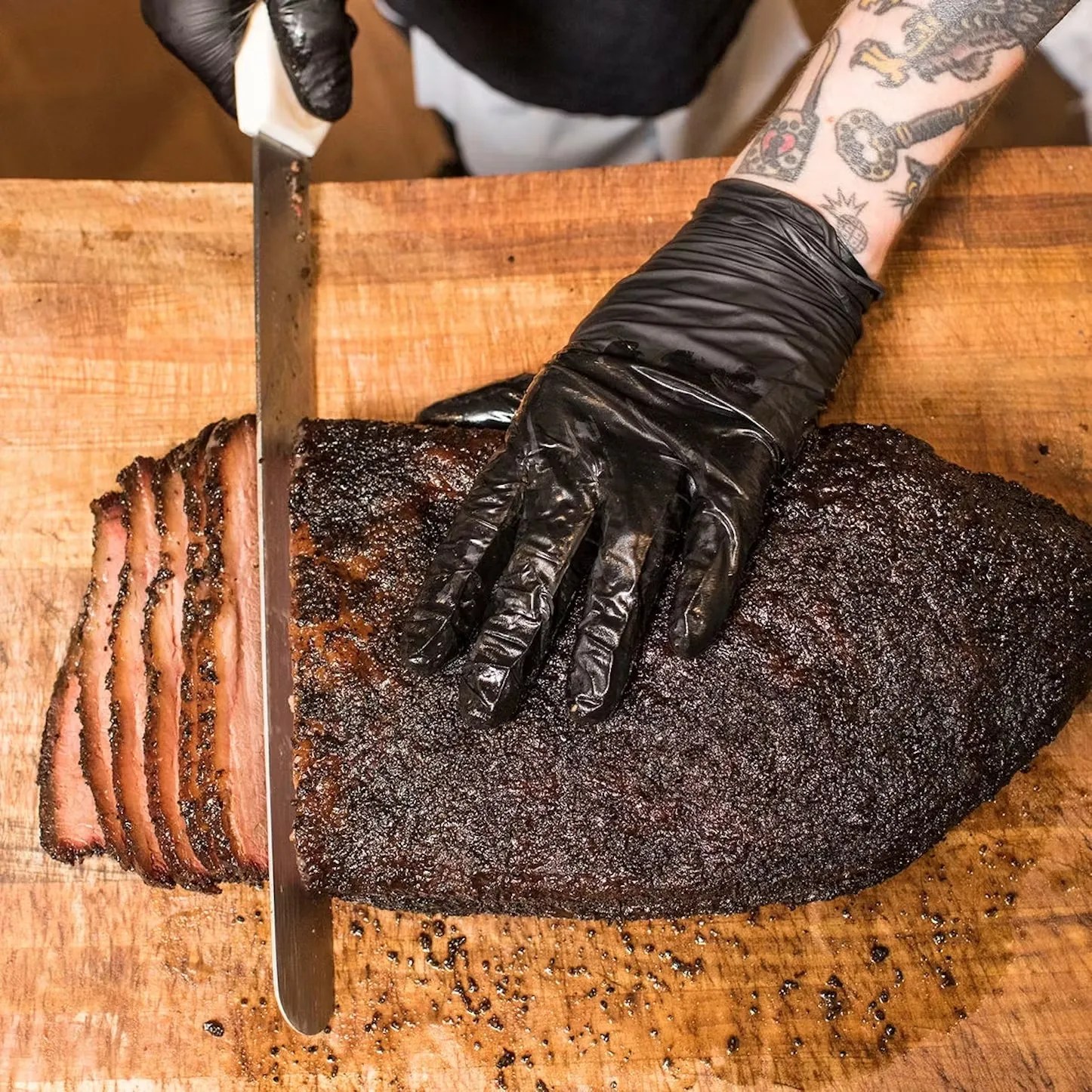 a tattooed man slices beef brisket