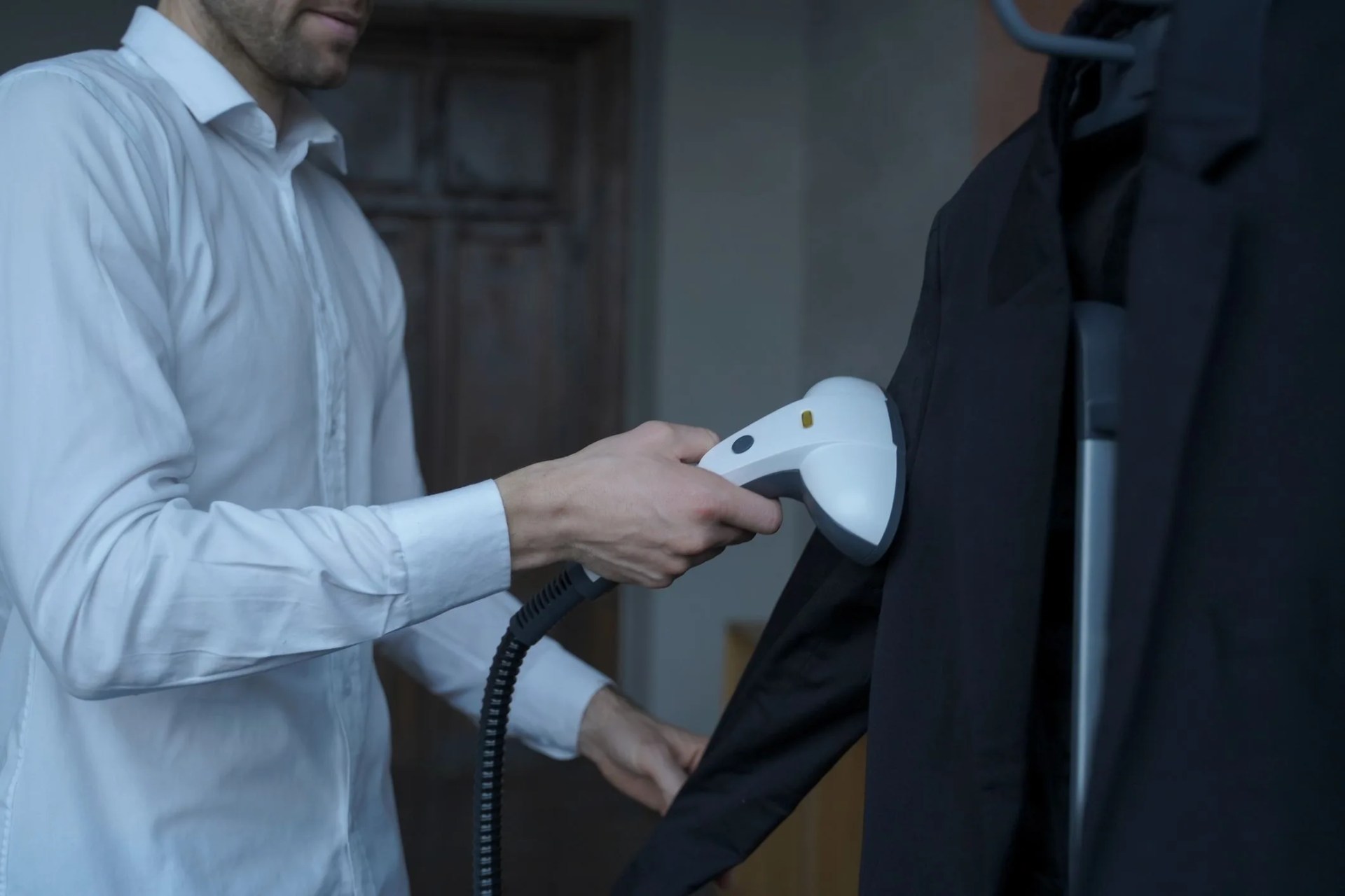 cropped photo of young businessman preparing himself for important meeting with partner, cleaning his suit with portable travel steamer, experienced office worker steaming formal clothes in morning