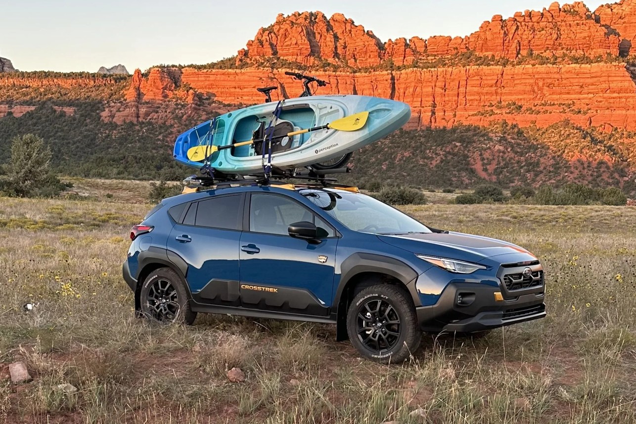 a car with a boat on top of it in a field with mountains in the background