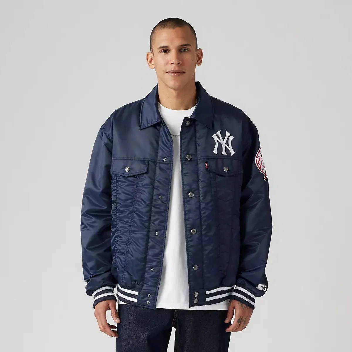 Male model wearing Levi’s x starter shirt jacket collaboration. The jacket is for the New York Yankees and is in the team’s colors of Navy and White with a large New York Yankee’s logo on the breast.