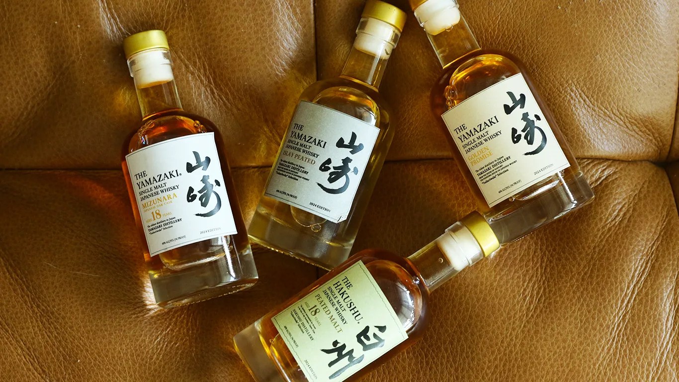 Miniature bottles of the 2024 Yamazaki Tsukuriwake collection laying flat on a leather couch surface.