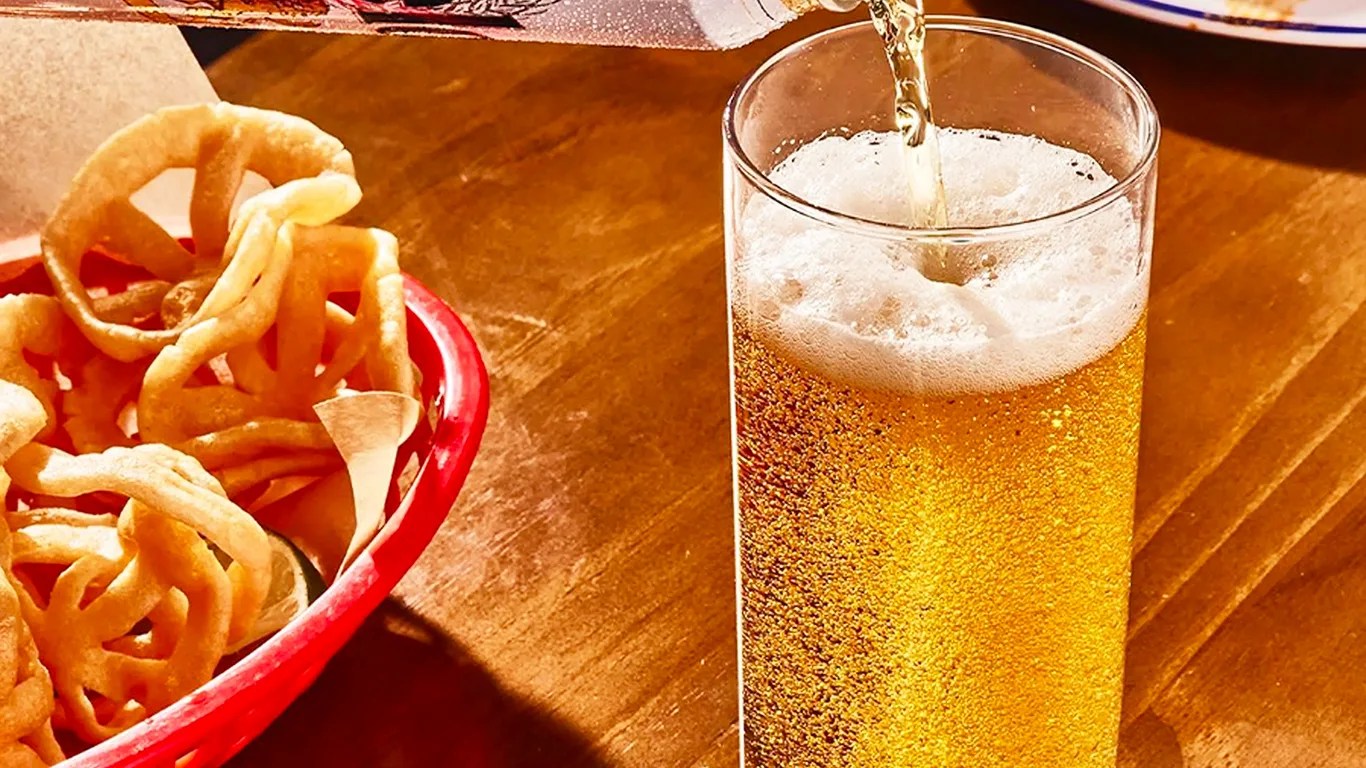 modelo beer being poured into a glass next to a basket of onion rings