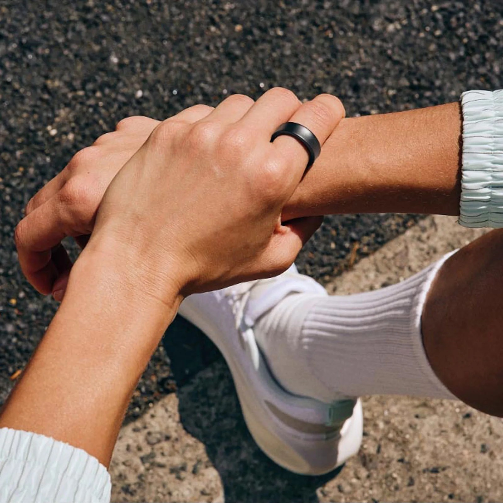 Samsung Galaxy ring worn on index finger of a person sitting with their arms crossed against a pavement background