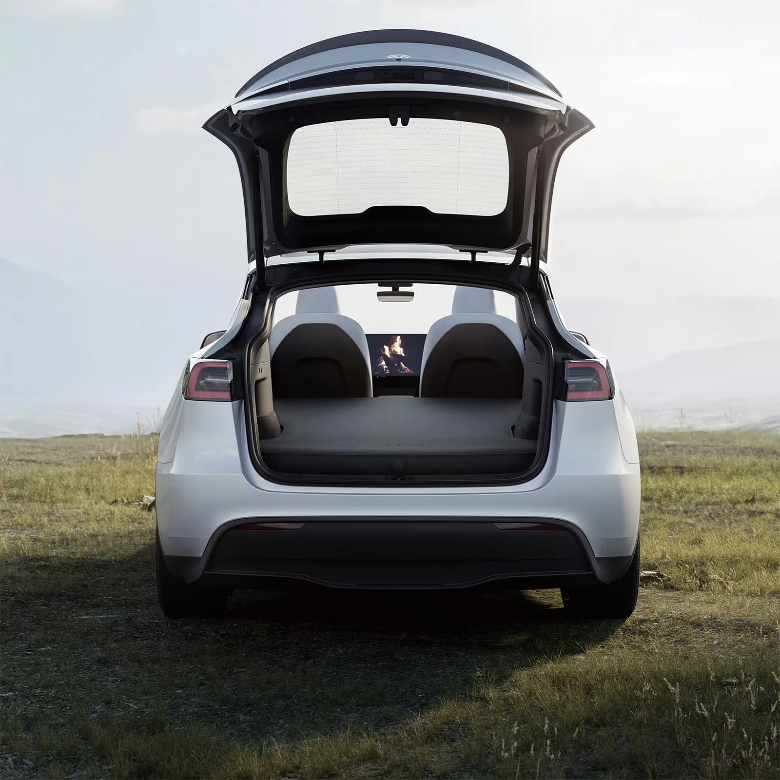 Tesla Model Y rear parked in a grass field shown with tailgate open to reveal the Tesla Model Y inflatable air mattress setup over the back seats and trunk area.