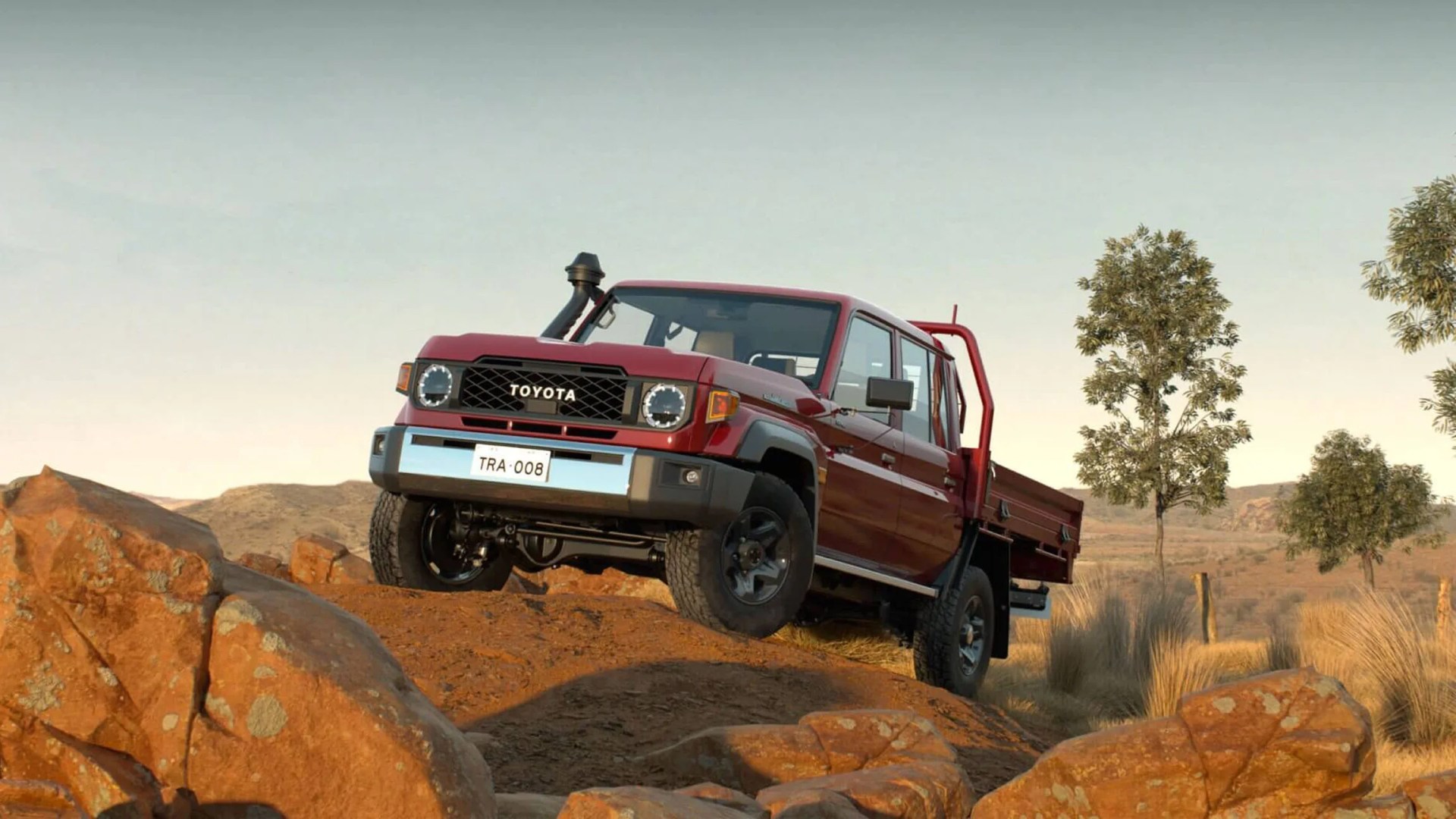 A truck bed version of Land Cruiser 70 series in red color with its front wheels perched on rocks in a desert setting.