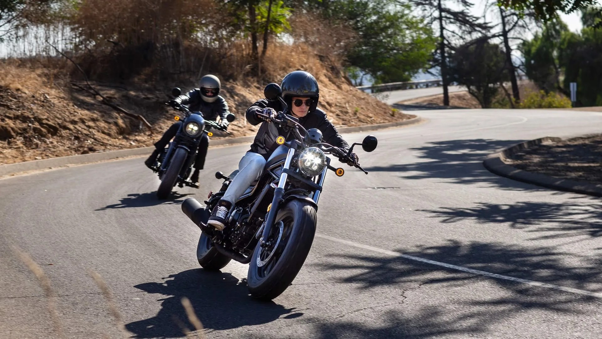 two people riding motorcycles on a curvy paved road