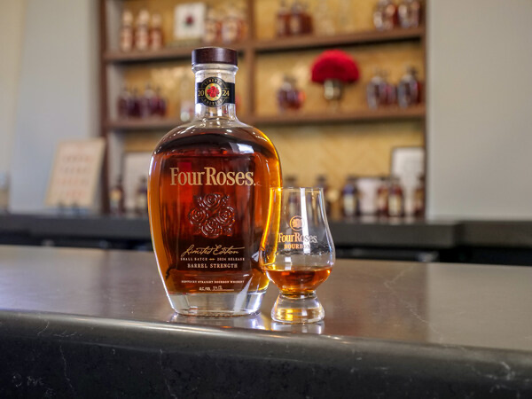 A bottle of the 2024 edition of Four Roses Limited Edition Small Batch Bourbon sitting on a bar next to a filled glencarin glass. 